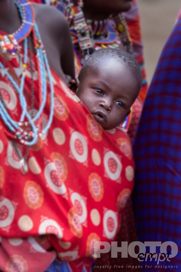 African Safari - Kenya. . . . . Closeup of Masai baby being carried in red and white shuka on young woman's hip, Masai village, Kenya, Africa