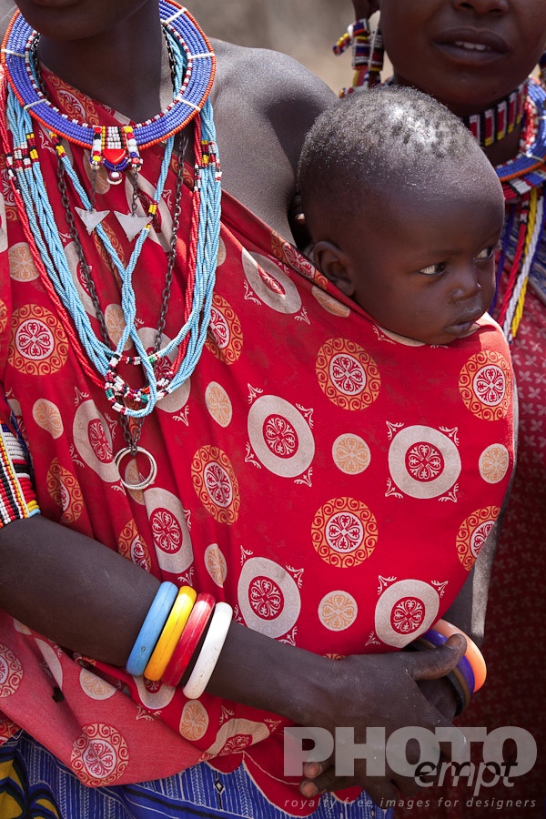 African Safari - Kenya. . . . . Closeup of Masai baby being carried in red and white shuka on young woman's hip, Masai village, Kenya, Africa