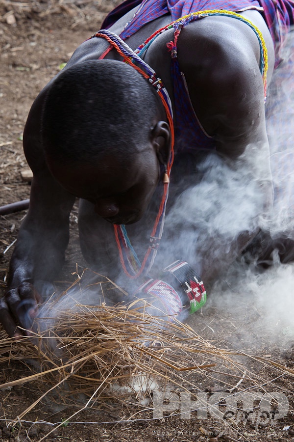 African Safari - Kenya. . . . . Closeup view of Masai warrior kneeling, starting fire using traditional method with sticks and dung, Masai village, Kenya, Africa