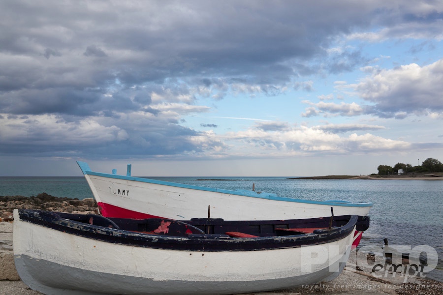 Italy South - Puglia. . . . . Beached wooden fishing boats on rocky shore, with skyscape at sunset, and headland across inlet in background, Puglia, Southern Italy