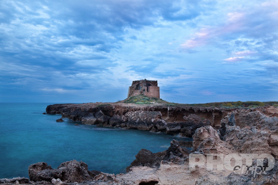 Italy South - Puglia. . . . . Rocky inlet near Brindisi, with medieval tower ruin, calm sea, and stormy skyscape at sunset,  Puglia, Southern Italy