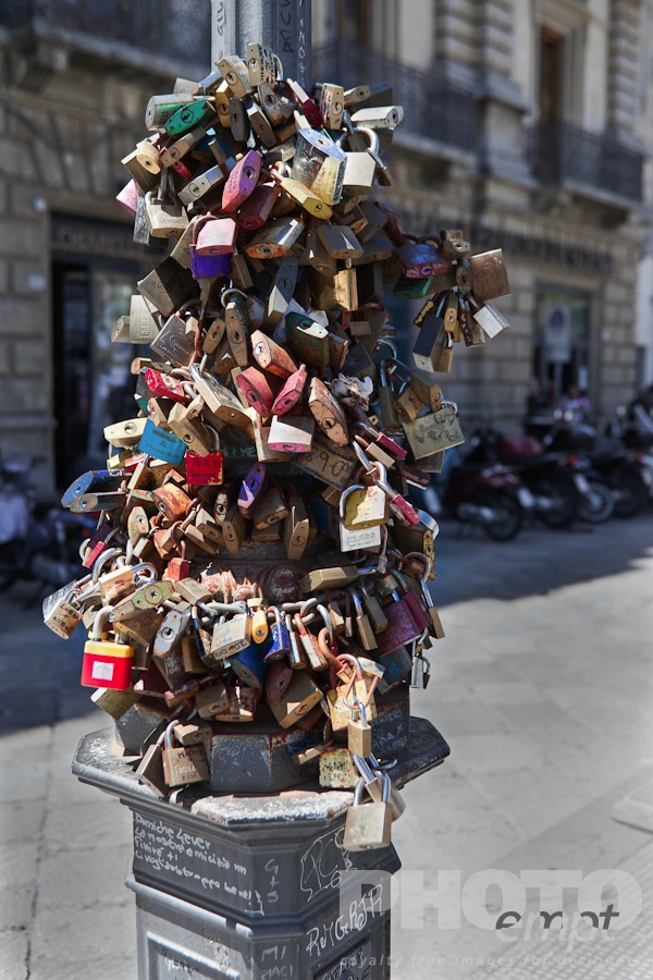 Italy South - Puglia. . . . . Padlocks fastened to chain on lamp post, multicoloured, against background of motorbikes parked outside Renaissance palazzo behind, Lecce, Salento, Puglia, Southern Italy