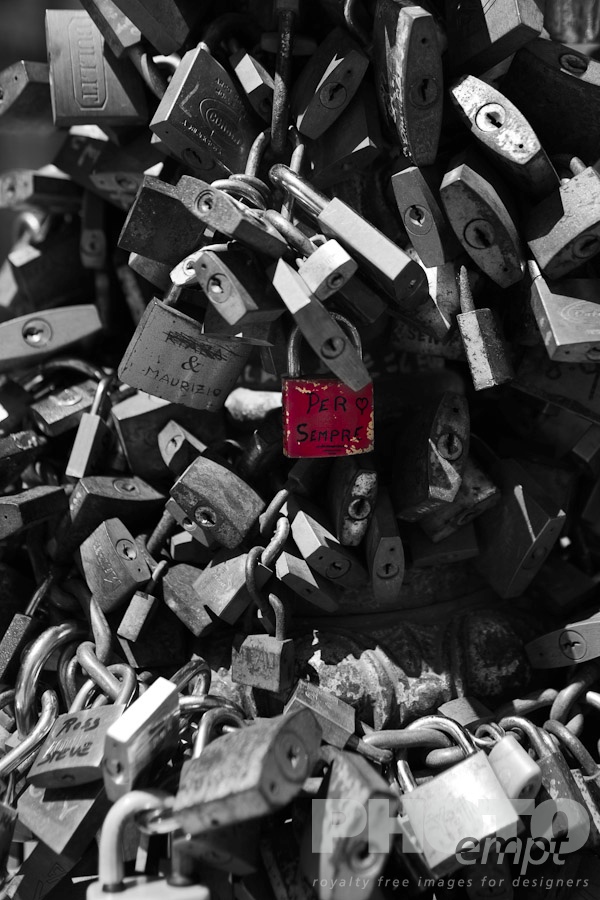 Italy South - Puglia. . . . . Monochrome close up view of multiple padlocks chained to lamp post, with central padlock in original red colour, inscribed with design of a heart and the message 