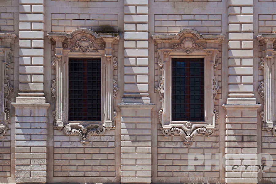 Italy South - Puglia. . . . . Window detail: ornate Baroque facade of Palazzo del Seminario, ornately carved in Leccese style, grid of metal bars across 2 windows, Lecce, Salento, Puglia, Southern Italy