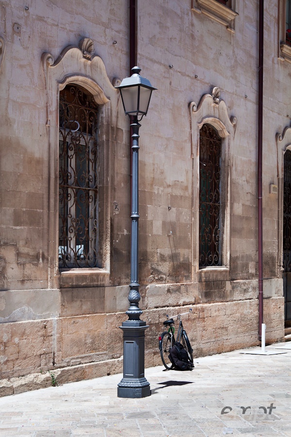 Italy South - Puglia. . . . . Sreet view detail with facade of  Renaissance palazzo, wrought iron grille over 2 windows, metal lamp post, and parked bicycle against palace wall, Lecce, Salento, Puglia, Southern Italy