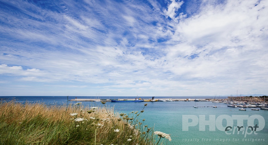 Italy South - Puglia. . . . . View of Otranto harbour with moored sailboats, cargo boat, and motorboats, sunny spring morning with dramatic clouds in blue sky, Salento, Puglia, Southern Italy