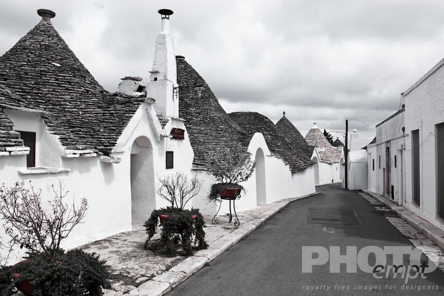 Italy South - Puglia. . . . . Street view: town of Alberobello, World Heritage site, with trullo houses, white painted stone with piled stone conical roofs with large chimneys, paved street and planters set against monochrome view,  Puglia, Southern Italy