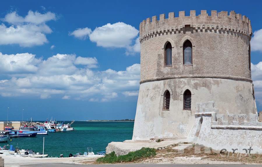 Italy South - Puglia. . . . . Typical defense castle of 16th century with rounded stone tower, overlooking harbour with moored fishing boats, sunny spring morning with blue sky, Salento, Puglia, Southern Italy