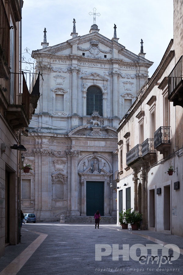 Italy South - Puglia. . . . . Facade of church of Sant'Irene , exuberant Baroque ornamentation of facade, street with single female figure in distance, sunny spring morning, Lecce, Salento, Puglia, Southern Italy