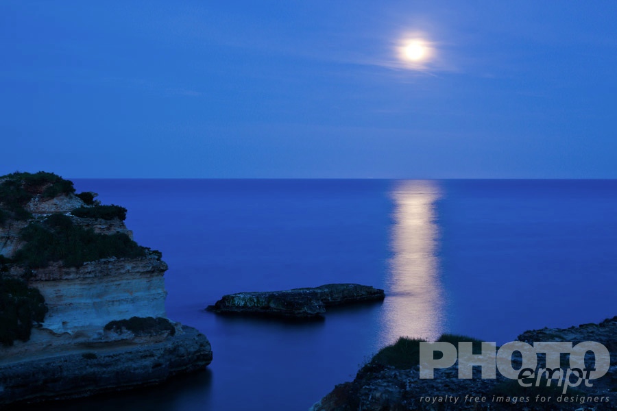 Italy South - Puglia. . . . . Cliffs and rocky coastline of Salento at twilight, with full moon reflection on calm sea, Puglia, Southern Italy