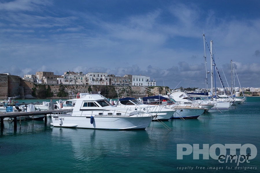 Italy South - Puglia. . . . . View of Otranto harbour with moored sailboats and motorboats, medieval fortifications and town beyond, sunny spring morning with blue sky, Salento, Puglia, Southern Italy