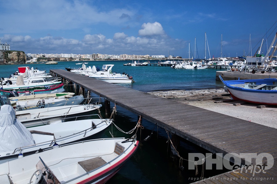 Italy South - Puglia. . . . . View of Otranto harbour with moored sailboats and motorboats, medieval fortifications and town beyond, sunny spring morning with blue sky, Salento, Puglia, Southern Italy