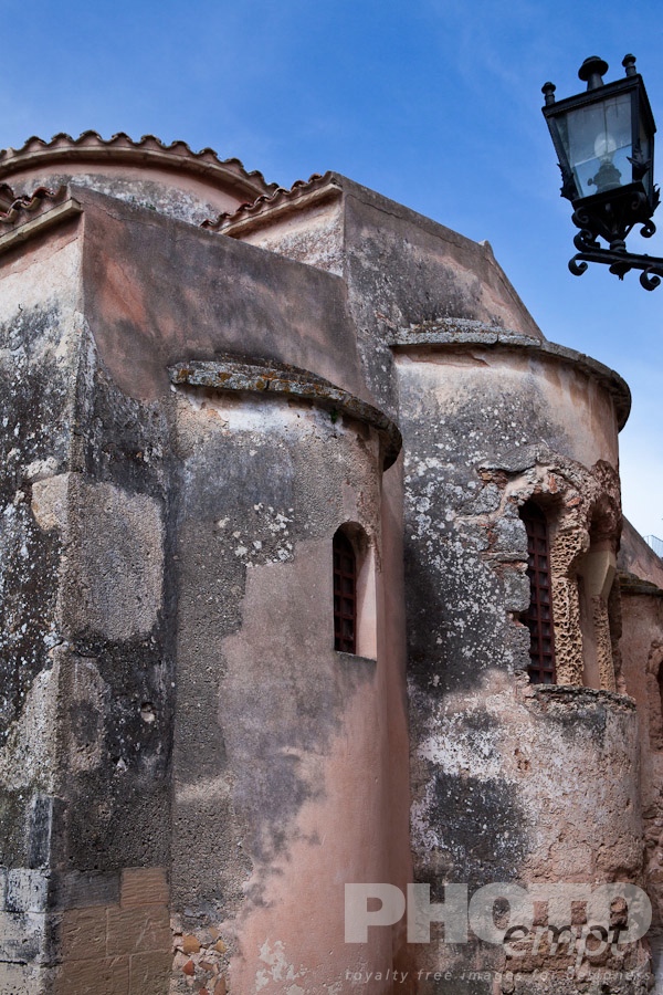 Italy South - Puglia. . . . . C;ose up view of exterior pink stone and plastered walls and apse, medieval church of San Pietro, Otranto,  with wrought iron street lamp, sunny spring morning with blue sky, Salento, Puglia, Southern Italy