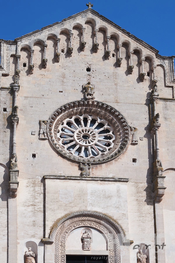 Italy South - Puglia. . . . . Detail of Romanesque facade of Duomo, with typical stone carved scroll work and statues around rose window, and arched decorated doorway, sunny spring afternoon, Matera, Puglia, Southern Italy