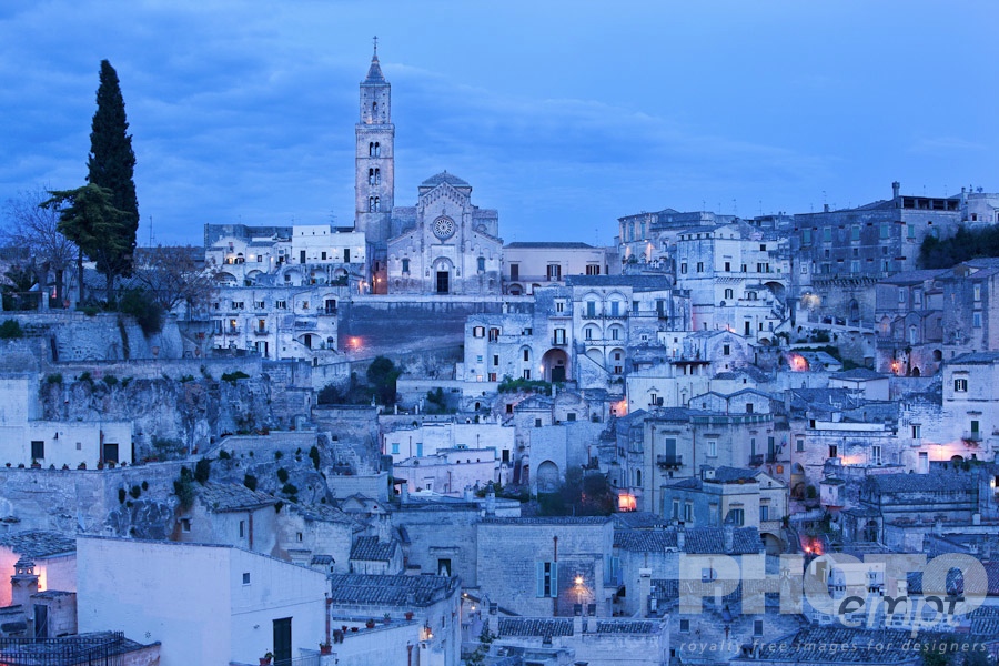 Italy South - Puglia. . . . . Aerial panorama of ancient town of Matera with tufa houses, Duomo and Campanile on hill beyond, at dusk with night illumination, Puglia, Southern Italy,