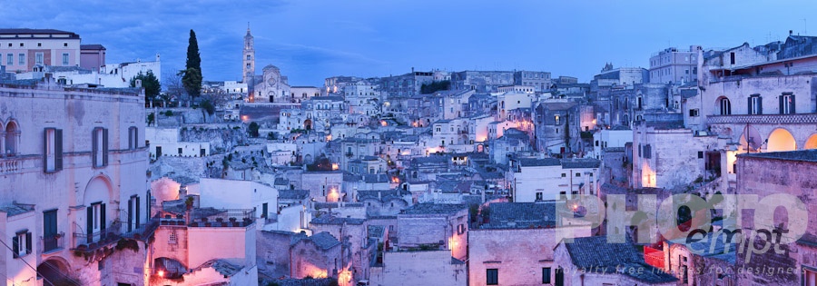 Italy South - Puglia. . . . . Aerial panorama of ancient town of Matera with tufa houses, Duomo and Campanile on hill beyond, at dusk with night illumination, Puglia, Southern Italy,