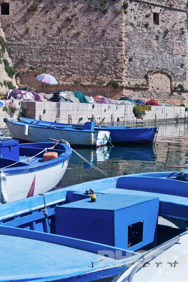 Italy South - Puglia. . . . . Wooden fishing boats moored in harbour, with fishing nets on quayside below the medieval walls of Gallipoli, sunny spring morning, Salento, Puglia, Southern Italy