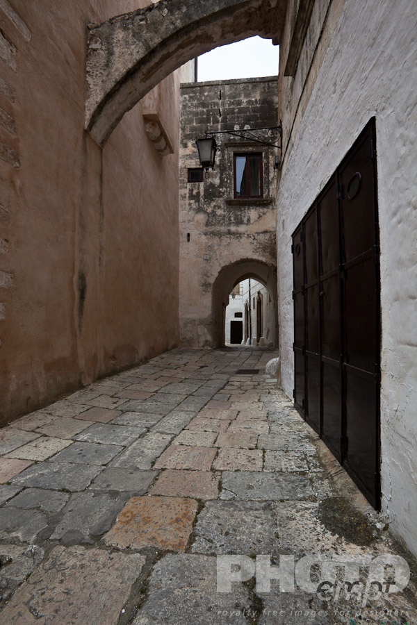 Italy South - Puglia. . . . . Street in Ostuni, with typical white stucco walls, stone paving, wrought iron lamp, and archway, spring afternoon, Salento, Puglia, Southern Italy