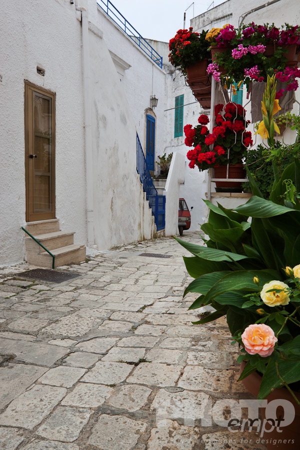 Italy South - Puglia. . . . . Street in Ostuni, with typical white stucco walls, stone paving, wrought iron lamp, and archway, with flowers decorating, spring afternoon, Salento, Puglia, Southern Italy