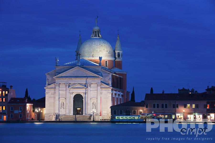 Venice in Autumn. . . . . View of church of Il Redentore, at twilight, with motion blur of passenger ferry, and water of Canale della Giudecca, lights illuminated along quayside, autumn in Venice, Northern Italy