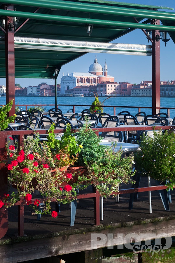 Venice in Autumn. . . . . View of Canale della Giudecca, looking towards church of Il Redentore, in late afternoon, with empty outdoor restaurant decorated with boxes of red flowers in foreground, autumn in Venice, Northern Italy